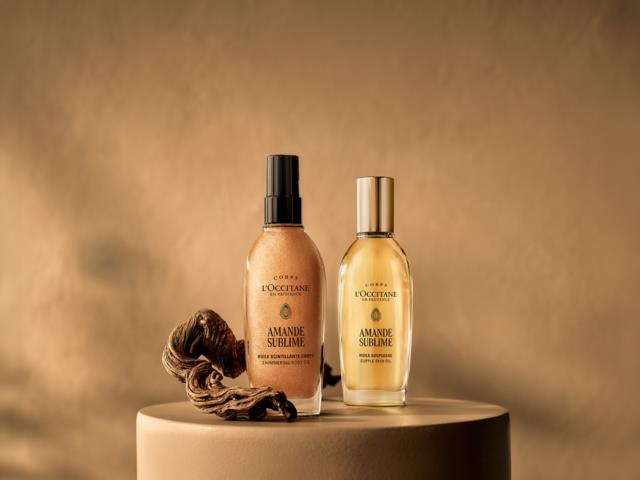 Two bottles of L'Occitane Amande Sublime products with a hair curl near the bottles on a round platform.