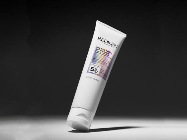 Redken hudvårdsprodukt i tub med lila, svart och vitt text, står på mörk bakgrund.