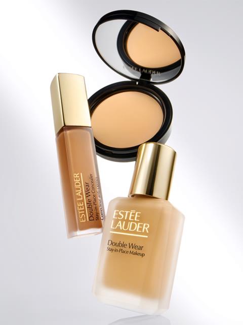 Två Estée Lauder Double Wear makeupflaskor, en kompakt med spegel, alla med guldlock och beige toner.