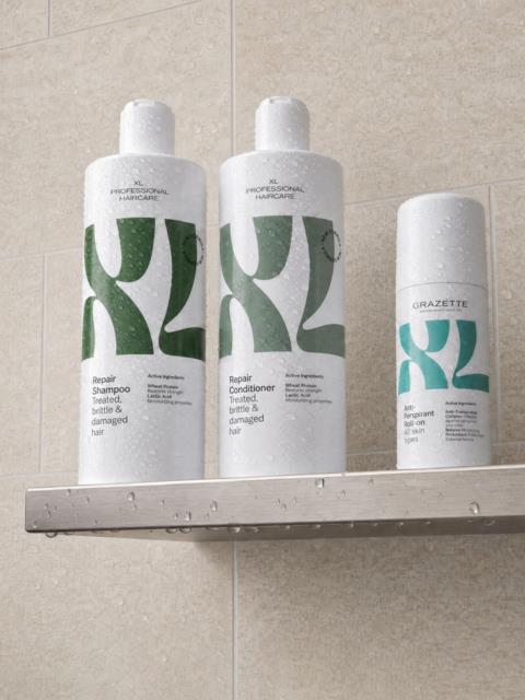 Tre hvite flaske med hårpleieprodukter med grønne og blå design på en flislagt badregal.